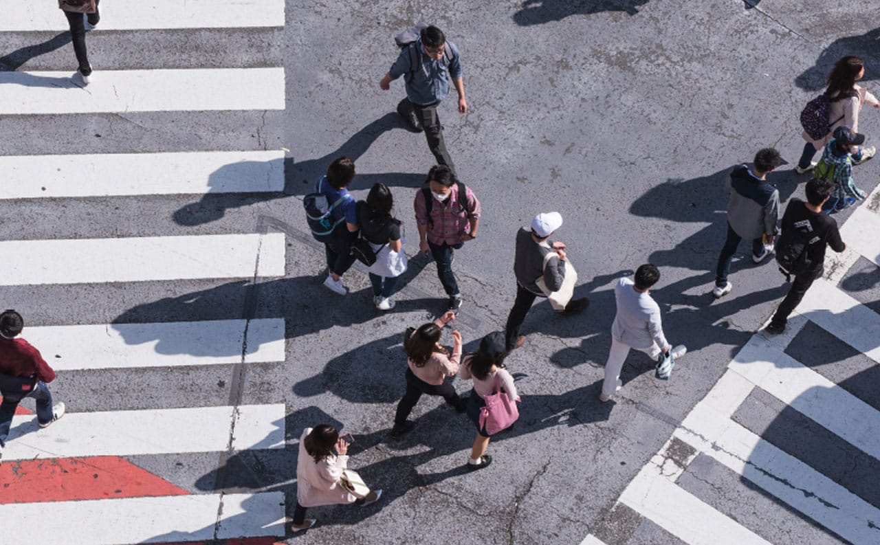 Foto di una folla di persone viste dall'alto che camminano su una strada asfaltata con strisce pedonali per rappresentare il modulo anagrafiche del CRM per Centri Acustici