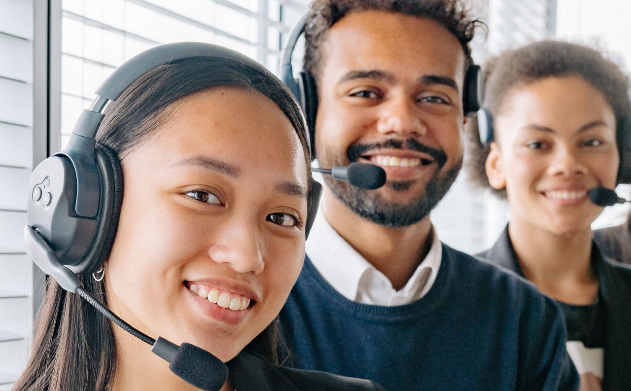 Foto in primo piano di tre centralinisti sorridenti con cuffie e microfono, vestiti eleganti, per rappresentare il modulo appuntamenti che gli Audioprotesisti possono utilizzare sul CRM Cosmo.